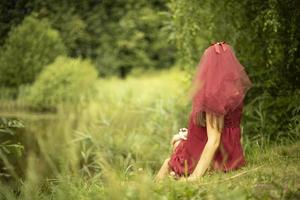 Girl on nature. Girl in dress sitting in grass. Red dress on woman. photo