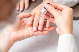 Manicurist pours oil on nails of woman photo