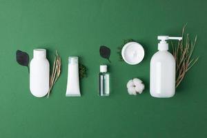 Cosmetic composition with cosmetic skin care products and flowers on green background. Flat lay, copy space photo