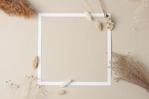 White frame with flovers on beige background. Flat lay, copy space. photo