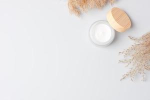 Jar of cosmetic cream with pampas dry grass on white background. Flat lay, copy space photo