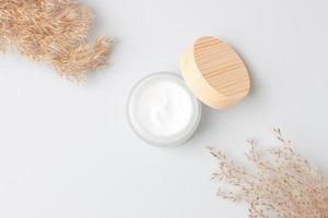 Jar of cosmetic cream with pampas dry grass on white background. Flat lay, copy space photo