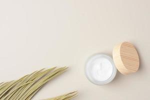 Jar of cosmetic cream with palm leaf on pastel beige background. Flat lay, copy space photo