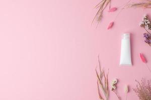 White tube of cosmetic cream with flowers on pink background. Flat lay, copy space photo