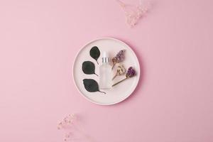 Cosmetic bottle with eucalyptus and plate on pink background. Flat lay, copy space photo