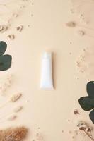 White tube of cosmetic cream with flowers on pastle beige background. Flat lay, copy space photo