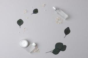 Skin care products on grey background with eucalyptus, flowers. Flat lay, copy space. photo