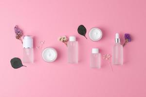 Skin care products on pink background with flowers, eucalyptus. Flat lay, composition. photo