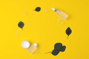 Skin care products on yellow background with flowers, eucalyptus. Flat lay, copy space. photo