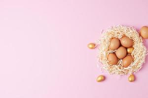 nido con huevos de pascua con flores sobre fondo rosa. endecha plana, espacio de copia foto