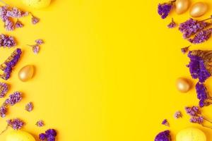 Easter yellow eggs with purple flowers on yellow background. Flat lay, copy space. photo