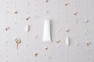 White tube of cosmetic cream with flowers on grey background. Flat lay photo