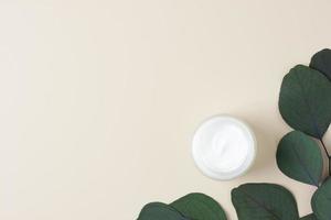 Jar of cosmetic cream with eucalyptus on pastel beige background. Flat lay, copy space photo