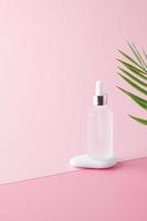 Cosmetic bottle with stone and palm leaf on pink background. Close up, copy space photo