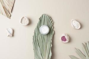 Jar of cosmetic cream and mask with palm leaf on pastel beige background. Flat lay photo