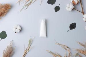 White tube of cosmetic cream with flowers on grey background. Flat lay photo