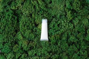 White tube of cosmetic cream on green moss natural background. Flat lay, copy space photo