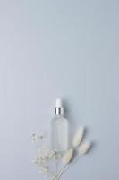 Cosmetic bottle with flowers on grey background. Flat lay, copy space photo