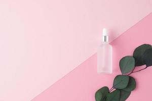 Cosmetic bottle with eucalyptus on pink background. Flat lay, copy space photo