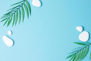 Spa background with white stones, water drops and palm leaves on blue. Flat lay,copy space photo