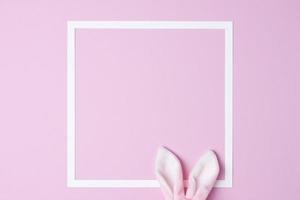 Bunny ears with white frame on pink background. Flat lay, copy space photo