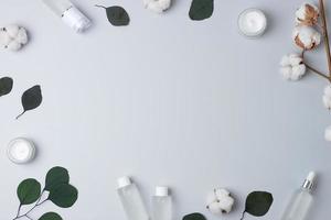 Cosmetic skin care products with flowers and eucalyptus on grey background. Flat lay, copy space photo