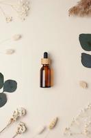 Cosmetic bottle with flowers and eucalyptus on pastel beige background. Flat lay photo