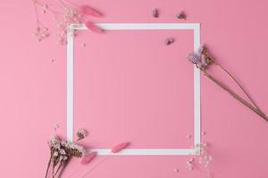 White frame with flowers on pink background. Flat lay, copy space. photo