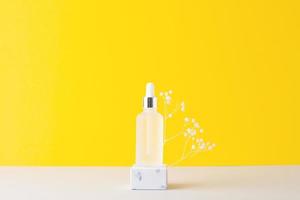 Cosmetic bottle with podium and flowers on yellow and grey background. Close up, copy space photo