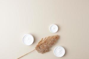 Jars of cosmetic cream with pampas on pastel beige background. Flat lay, copy space photo