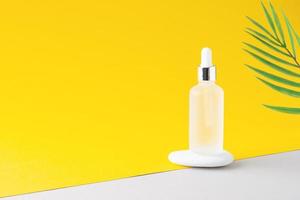 Cosmetic bottle with stone and palm leaf on yellow and grey background. Close up, copy space photo