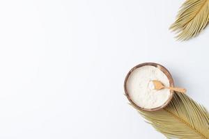 Collagen powder in bowl with measure spoon with palm leaves on white background. Flat lay, copy space photo