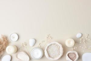 Spa composition with skin care products, stones, candles and flowers on pastel beige. Flat lay photo