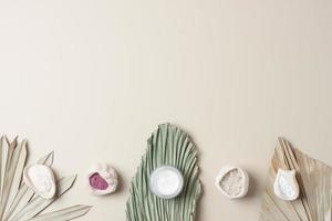 Jar of cosmetic cream and mask with palm leaf on pastel beige background. Flat lay, copy space photo
