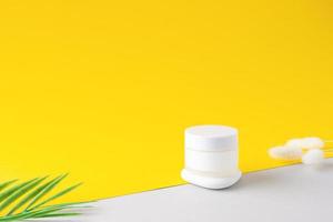 Jar of cosmetic cream with flowers and stone on yellow and grey background. Close up, copy space photo