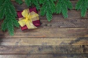 Red gift box with yellow bow on wooden background with Christmas tree branches. New Year. Copy space photo