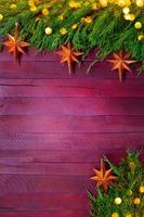 textura de tablas rojas y moradas con ramas de thuja verde y estrellas naranjas con bokeh amarillo. navidad, año nuevo. vertical. copie el espacio foto