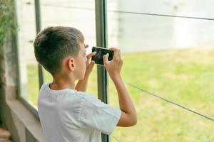 Boy photographs animals with smart phone in a zoo through protective glass photo