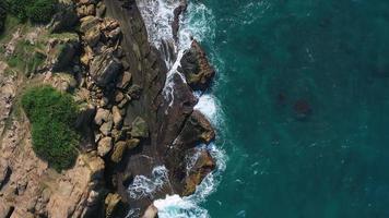 imágenes aéreas de 4k de vista superior por drones de olas azules del océano rompen en el alto acantilado de una montaña rocosa. olas de mar de peligro en una playa video