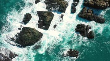 imágenes aéreas de 4k de vista superior por drones de olas azules del océano rompen en el alto acantilado de una montaña rocosa. olas de mar de peligro en una playa video