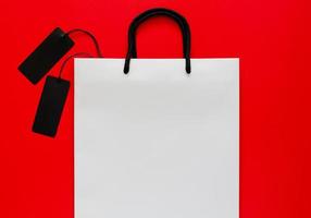 White shopping bag with black price tags on red background. Black friday concept. photo