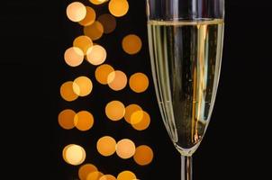 Partial focus of a glass of sparkling wine with golden bokeh lights on dark background. photo