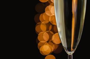 Partial focus of a glass of sparkling wine with golden bokeh lights on dark background. photo