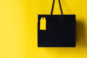 bolsa de compras negra con etiqueta de precio amarilla en blanco con fondo amarillo para el concepto de venta de compras de viernes negro. foto