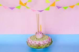 Pink lotus petal krathong that have 3 incense sticks and candle decorates with lotus and crown flower for Thailand Loy Krathong festival on pink and blue background. photo