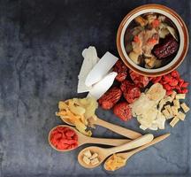 Top view of many chinese herbs with bowl of clear soup on black photo