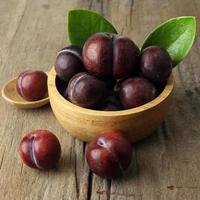 Close up of fresh plum fruits in bowl on wooden background photo