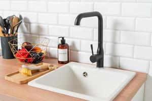 Kitchen sink on wooden countertop, white brick wall and black faucet photo