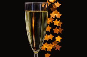 Blurred focus of a glass of sparkling wine with golden star shape bokeh lights on dark background. photo