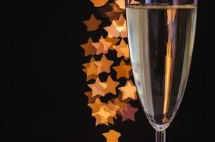 Partial focus of a glass of sparkling wine with golden star shape bokeh lights on dark background. photo